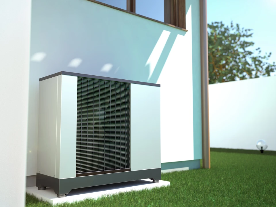 Technicien en climatisation travaillant sur une unité extérieure de pompe à chaleur devant un bâtiment moderne à bardage bois
