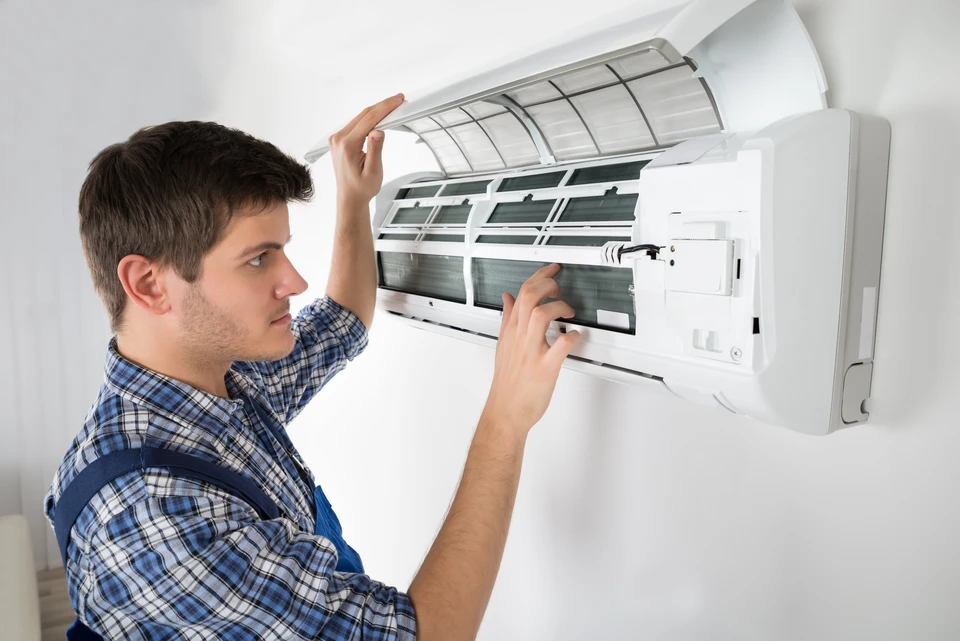 Technicien en salopette bleue effectuant la maintenance d'un climatiseur mural split system