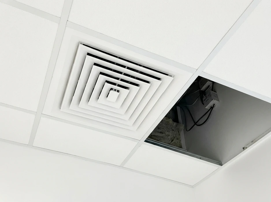 Plafond suspendu de type dalle acoustique avec diffuseur d'air carré à quatre cônes concentriques blancs, typique des systèmes CVC tertiaires