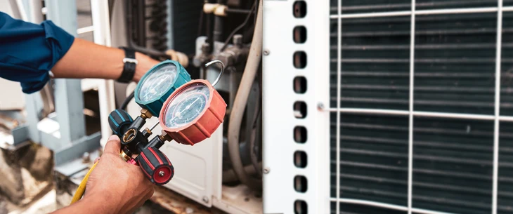 Un technicien assure l'entretien d'un climatiseur situé à côté d'une maison moderne
